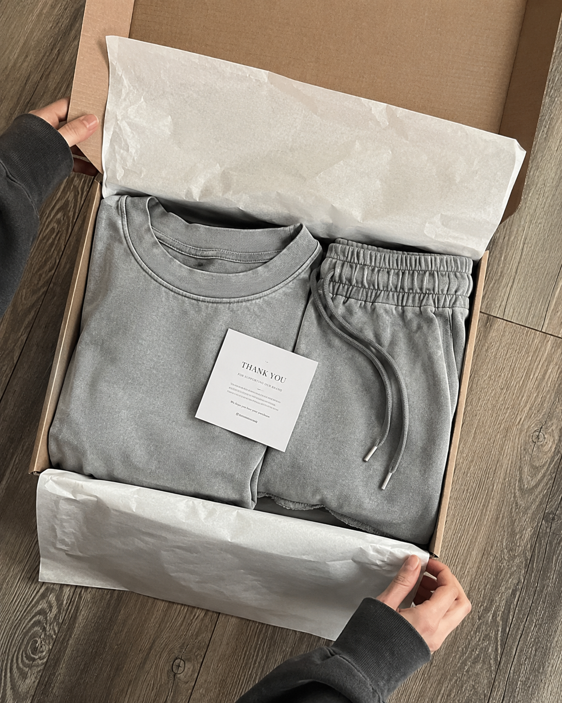 Conjunto gris empaquetado en caja kraft con tarjeta de agradecimiento.